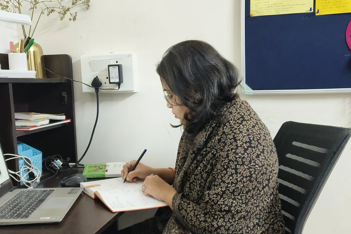 Shruti writing lesson notes beside her laptop